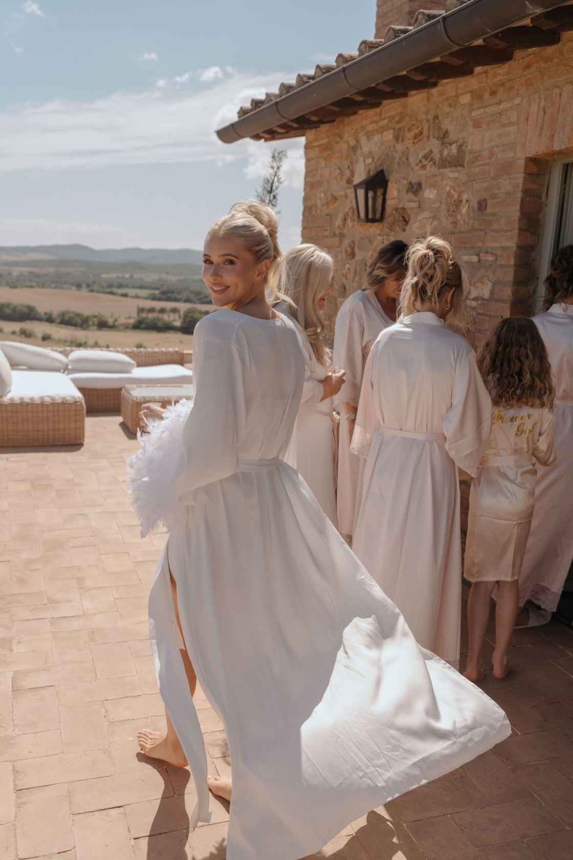 Fern glancing back over her shoulder on a terrace at Conti di San Bonifacio, bridesmaids in matching white robes and Maremma hills behind her